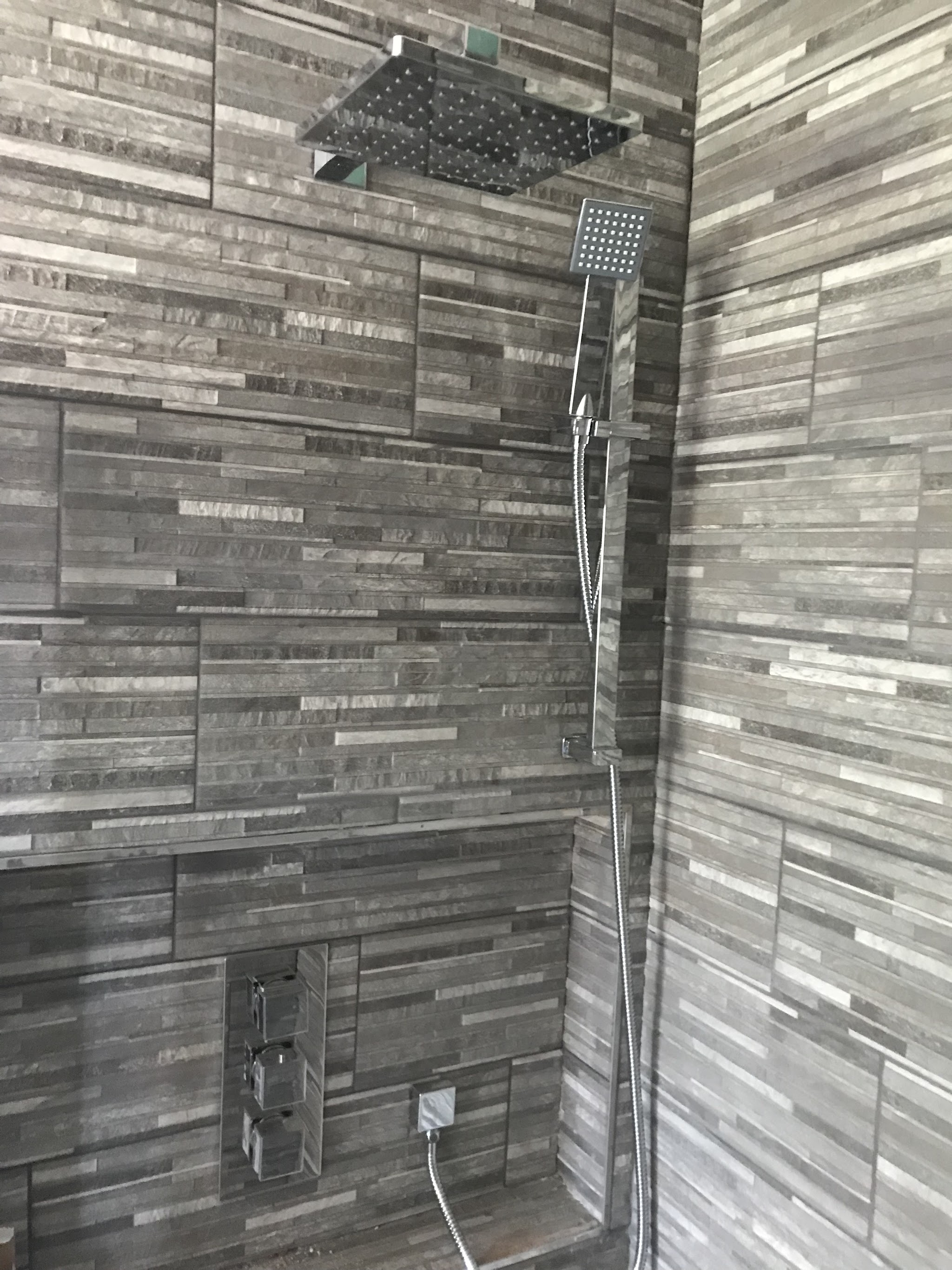Walk-in shower with grey split-face tiles and a square rainfall shower head