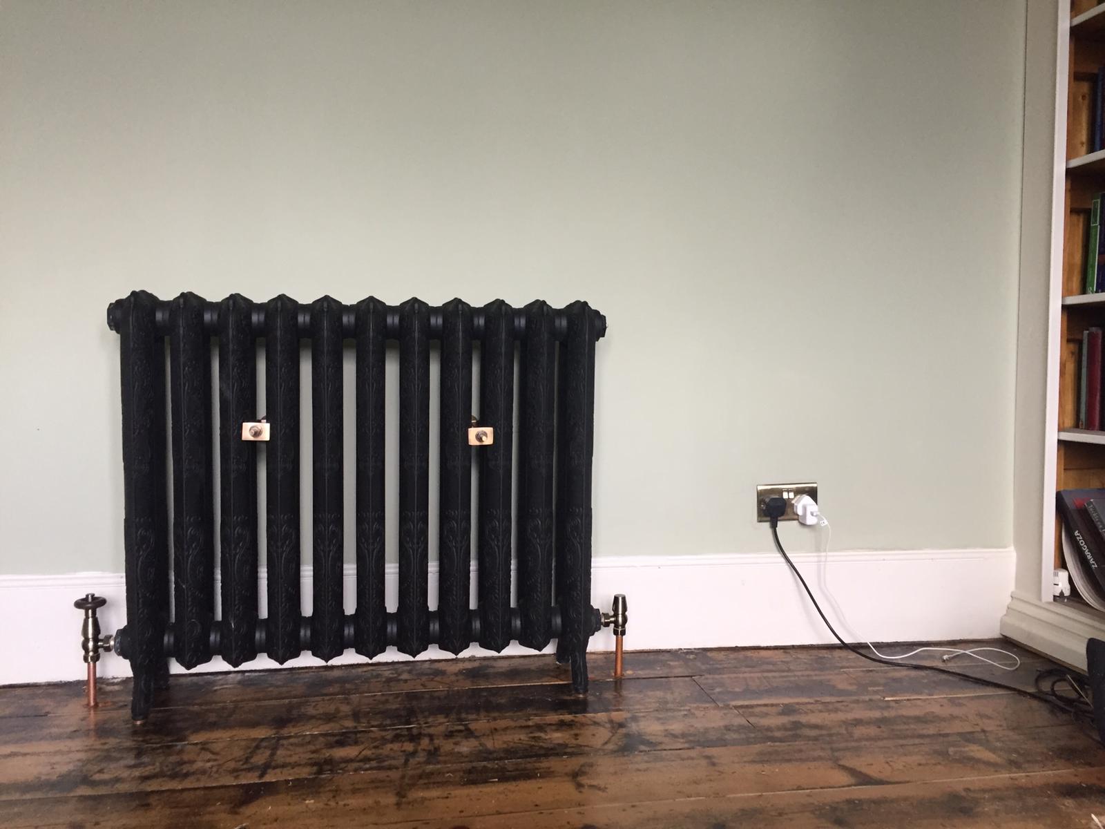 Black cast-iron column radiator with copper tails on period floorboards